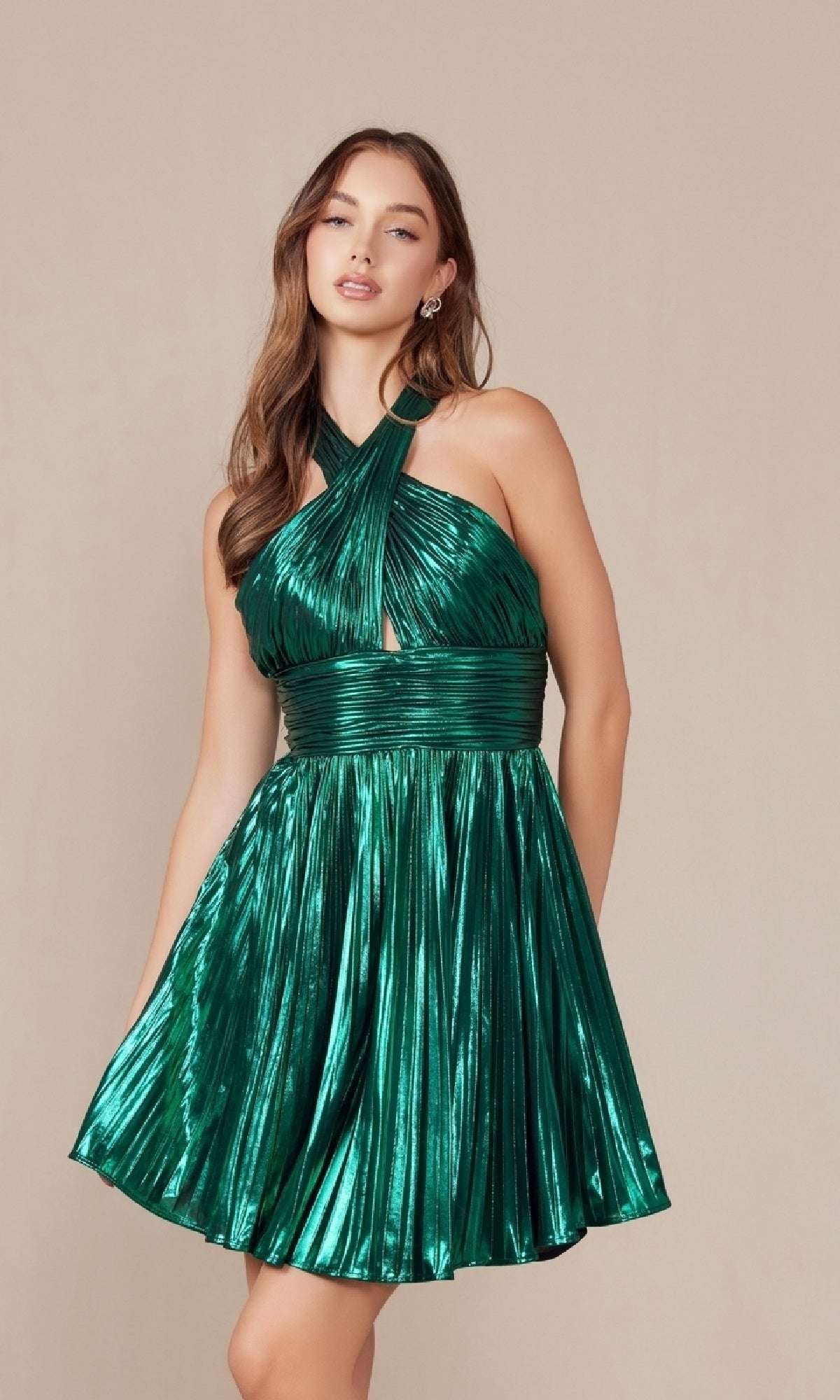 Woman in an affordable Short Metallic Cut-Out Halter Hoco Dress K822—shiny green, fitted waistband—stands against a plain beige background.